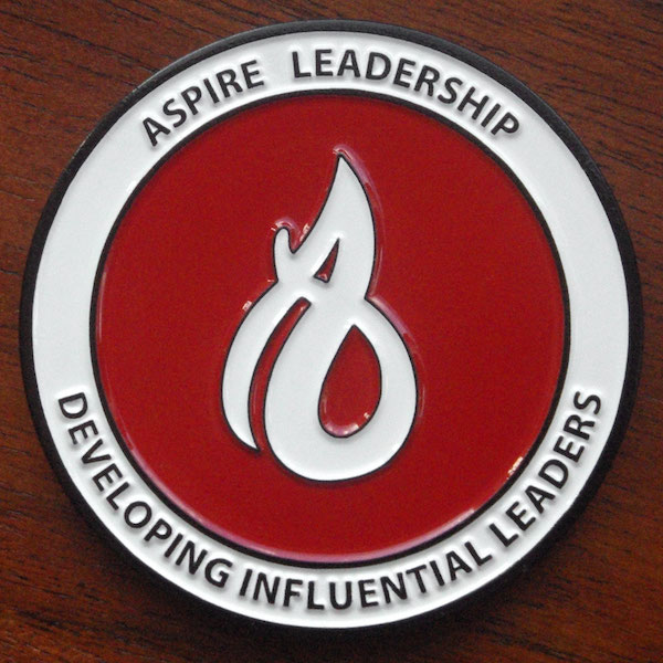 Round red and white challenge coin representing Aspire Leadership